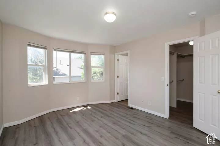 Spacious room featuring multiple windows, wood-finish flooring, light-toned walls, and a built-in closet with hanging rods