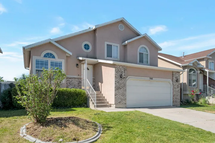 Two-story stucco and stone-faced residence featuring an arched window, a circular window, an attached two-car garage, concrete stairs with a metal handrail, and a concrete driveway