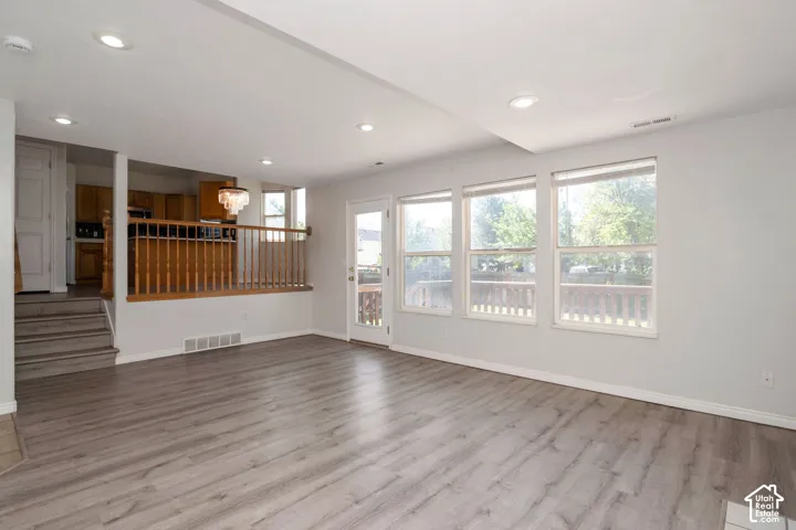 Spacious living area featuring light wood-finish flooring, recessed lighting, and a series of three large windows providing abundant natural illumination