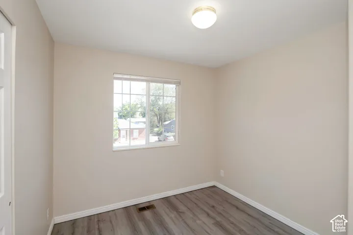 Neutral tone painted walls, wood-finish flooring, white window frame with horizontal blinds, white baseboards, and a flush-mount ceiling light fixture