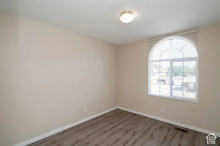 Room featuring a large arched window with blinds, neutral wall paint, and wood-finish flooring