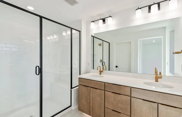 Bathroom featuring a dual vanity with wood-finish cabinetry, a white countertop, and gold-tone fixtures