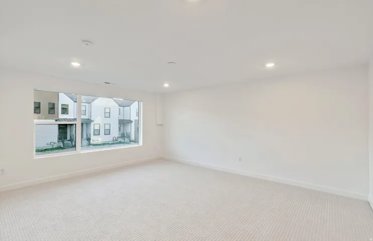 Spacious room featuring a large horizontal window, recessed ceiling lighting, light-toned carpeting, white baseboards, and neutral wall tones