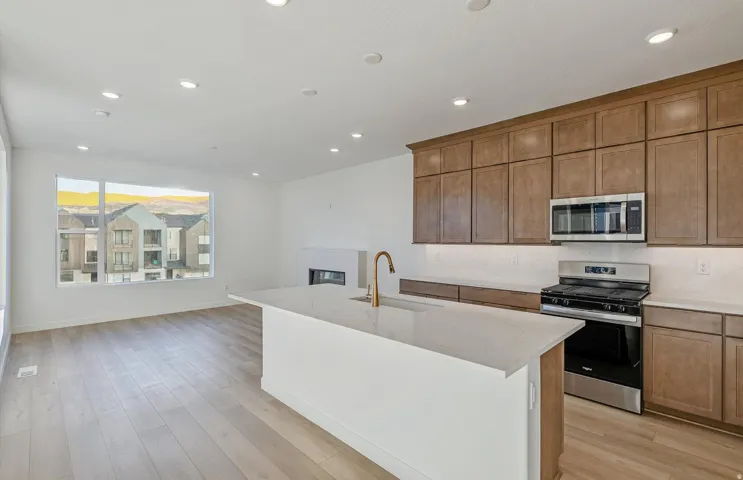 Open-concept living space featuring a kitchen island with sink, wood-finish flooring, recessed lighting, and a built-in fireplace