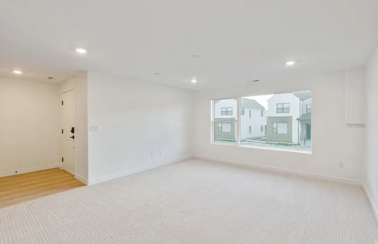Spacious interior featuring a large picture window, recessed lighting, neutral carpeting, and a light wood-finish flooring section