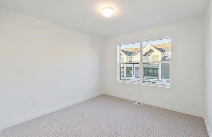 Neutral-toned room featuring a large window, light-colored carpeting, white baseboards, and a ceiling-mounted light fixture