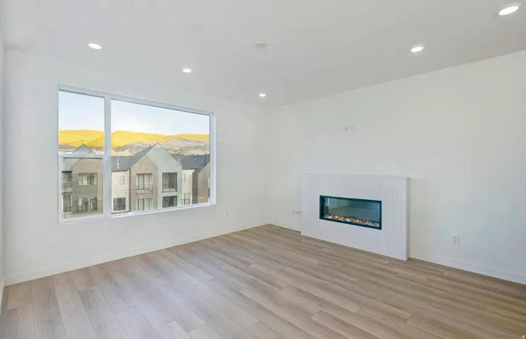 Spacious room featuring wood-finish flooring, a modern linear electric fireplace with a white mosaic tile surround, and a large picture window