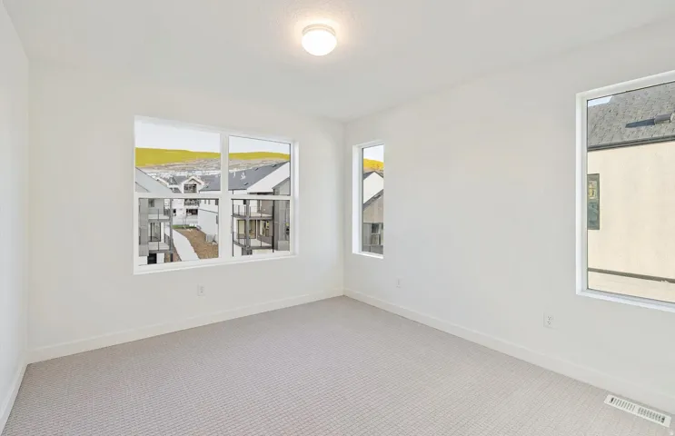 Bright room with multiple windows, light-colored walls, patterned carpeting, white baseboards, and a flush-mount ceiling light