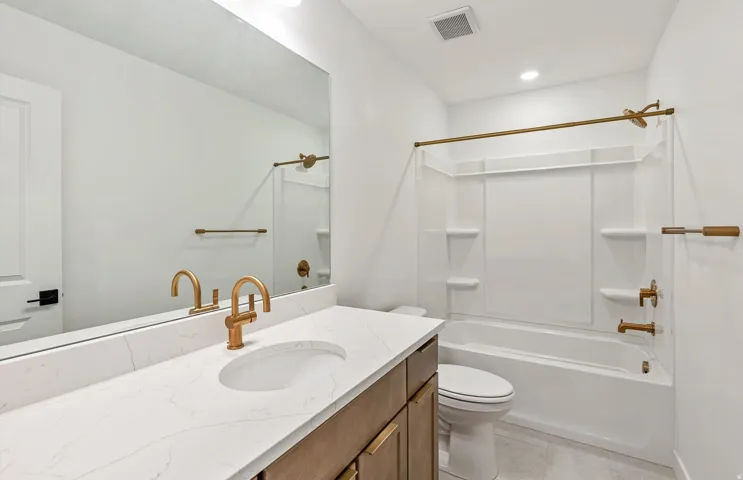 Bathroom featuring a vanity with a white stone-finish countertop, undermount sink, and brass-finish faucet