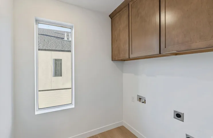 Utility space featuring a vertical window, wood-finish flooring, two upper cabinetry units, and utility hookups