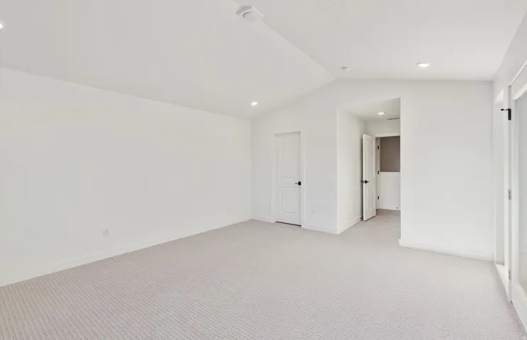 Spacious room featuring vaulted ceilings, light-toned carpeting, recessed lighting, and white baseboards