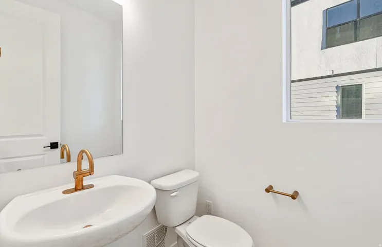 Contemporary powder room featuring a wall-mounted sink with a gold-finish faucet, a rectangular mirror, and a white framed window