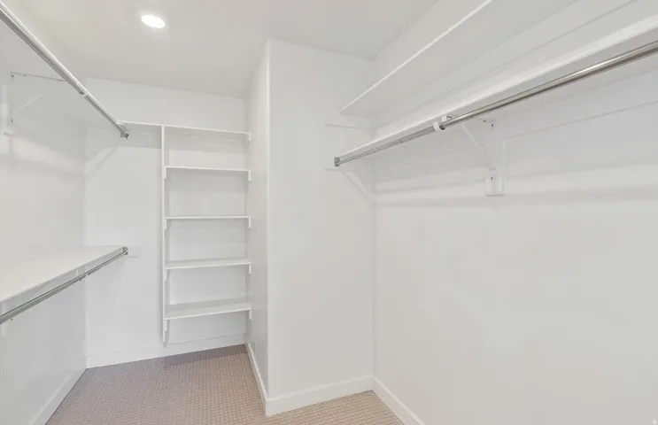 Walk-in closet featuring recessed lighting, white walls, built-in shelving, two hanging rods, and patterned carpet flooring