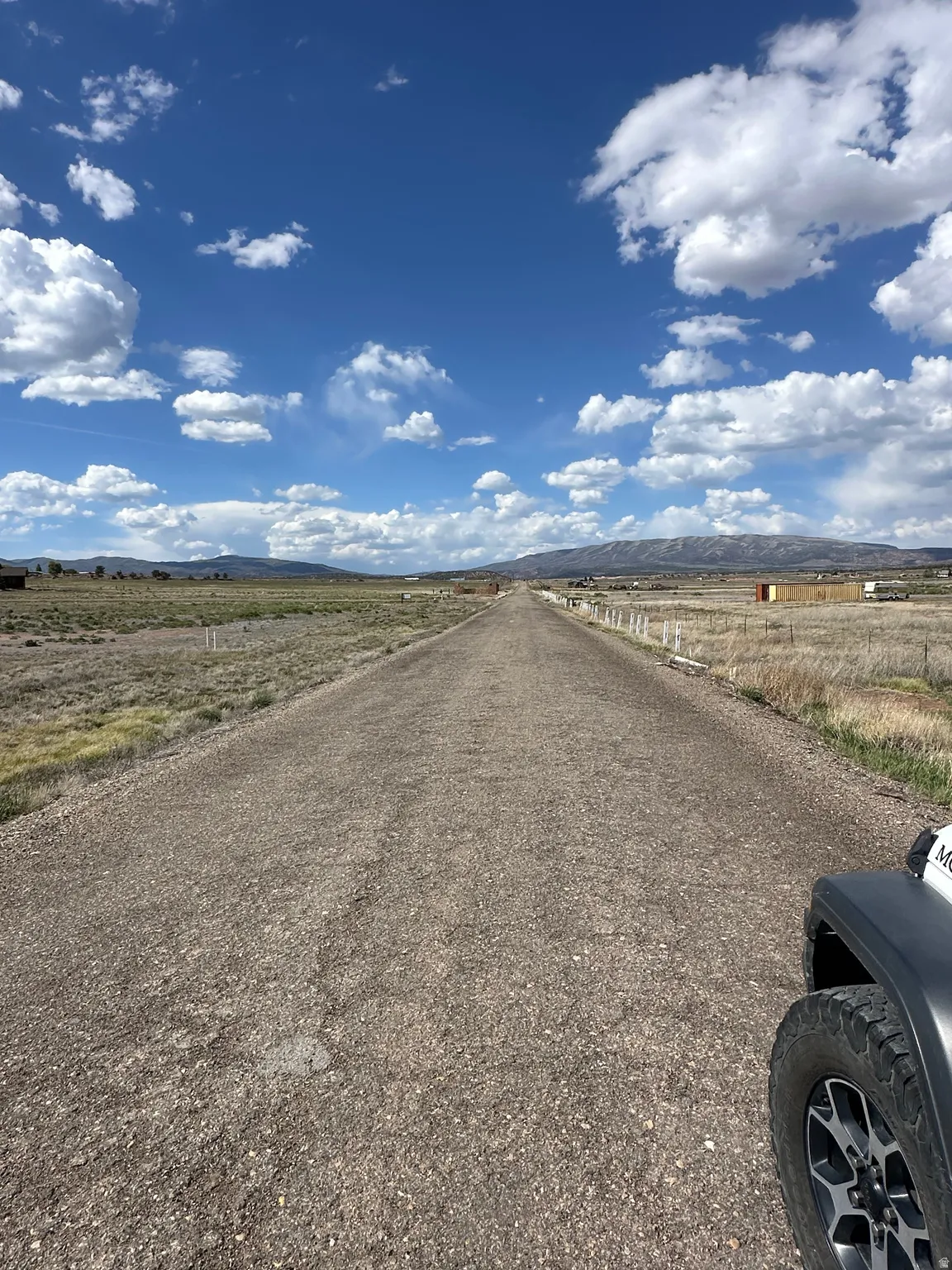 Gravel road extending into the distance, framed by open fields with sparse vegetation
