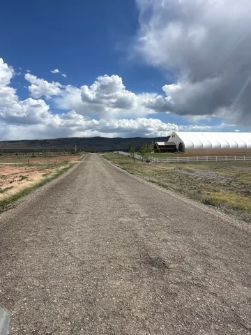 Gravel driveway leading to a multi-building property with a white fabric-covered structure and a white-sided building with a dark roof