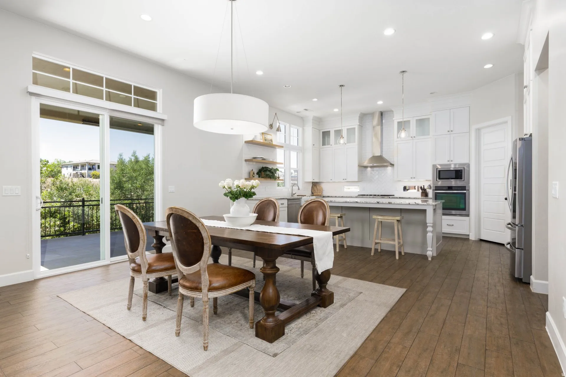 Open-concept living space featuring wood-finish flooring, a contemporary kitchen with white cabinetry and stainless steel appliances, a kitchen island with seating, a large dining area, and sliding glass doors leading to a balcony