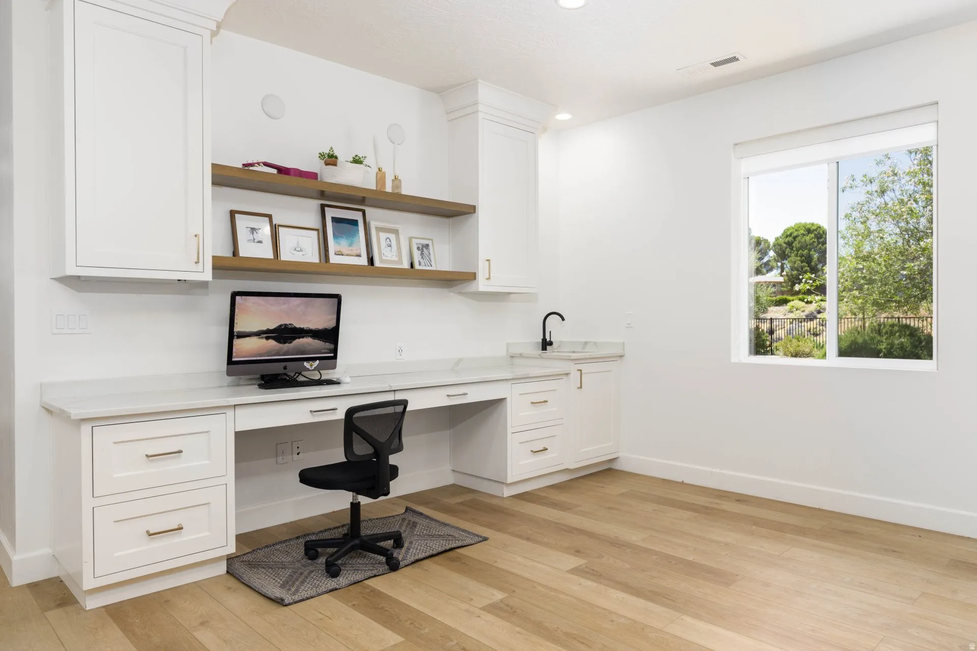 Built-in desk and cabinetry featuring a light-toned countertop, integrated sink with a matte black faucet, and open wood-finish shelving