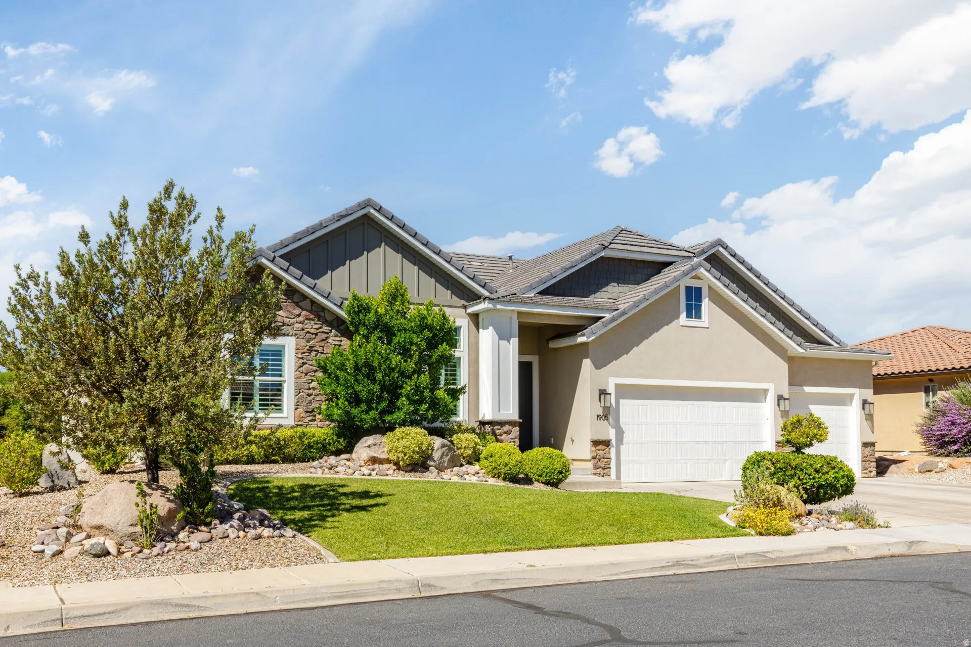 Contemporary stucco exterior featuring a stone facade accent, multi-gabled roofline, and attached two-car garage