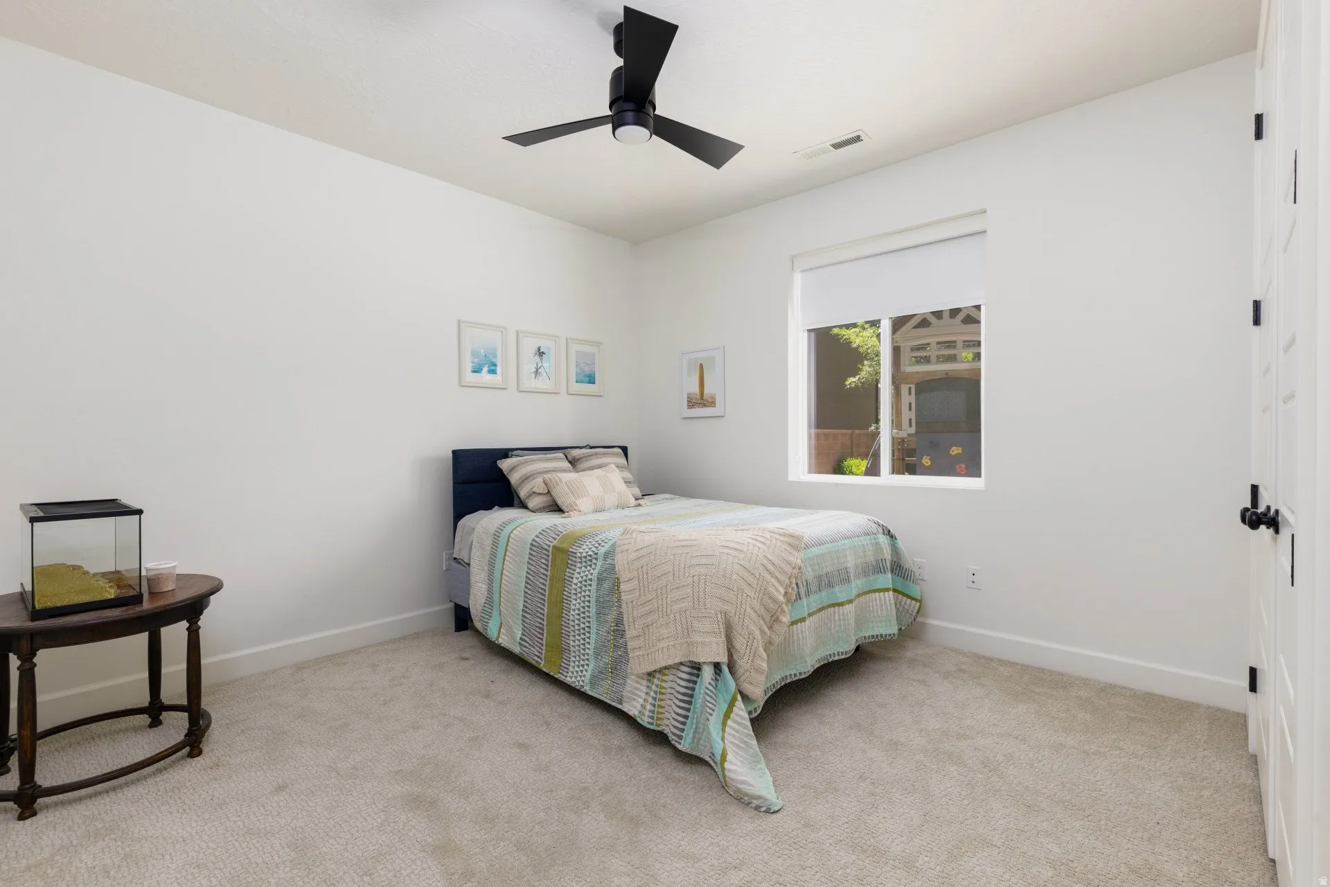 Carpeted room featuring a ceiling fan with black blades, a single window with a roller shade, white walls, and white trim