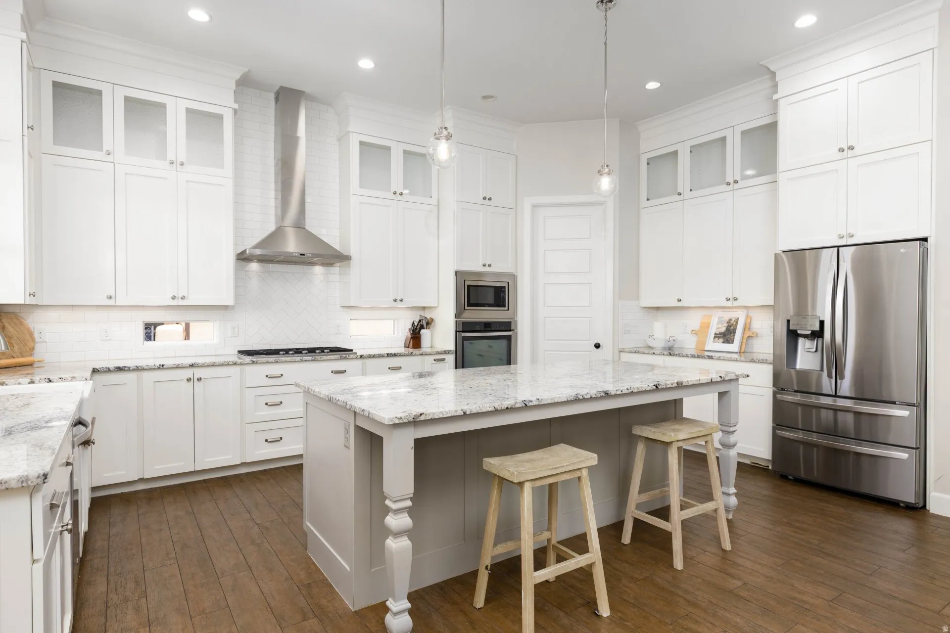 Bright kitchen featuring white cabinetry, granite countertops, a central island, stainless steel appliances, and wood-finish flooring