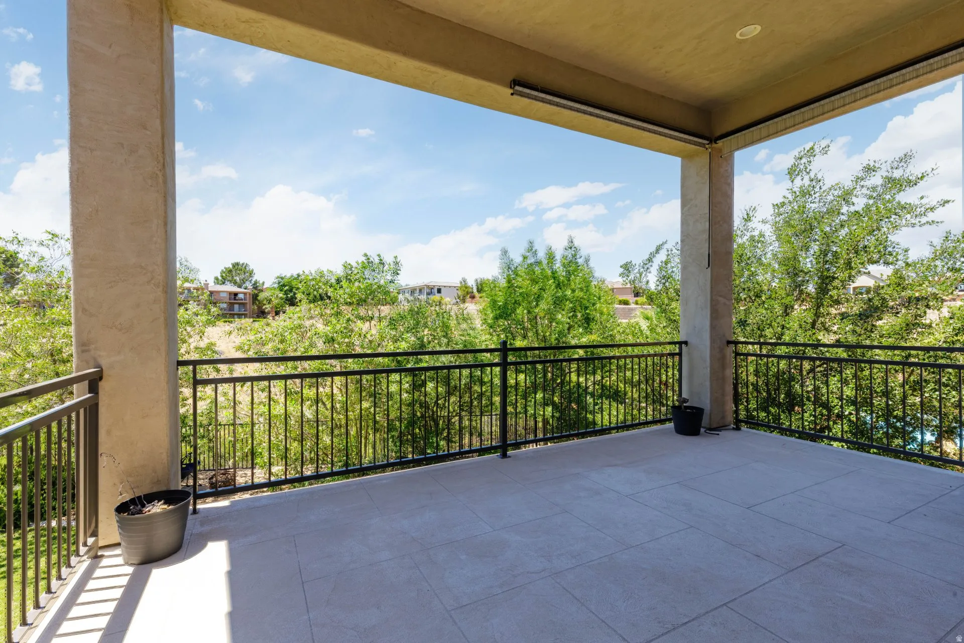Spacious covered patio featuring a tiled floor, black metal railings, recessed lighting, and stucco columns