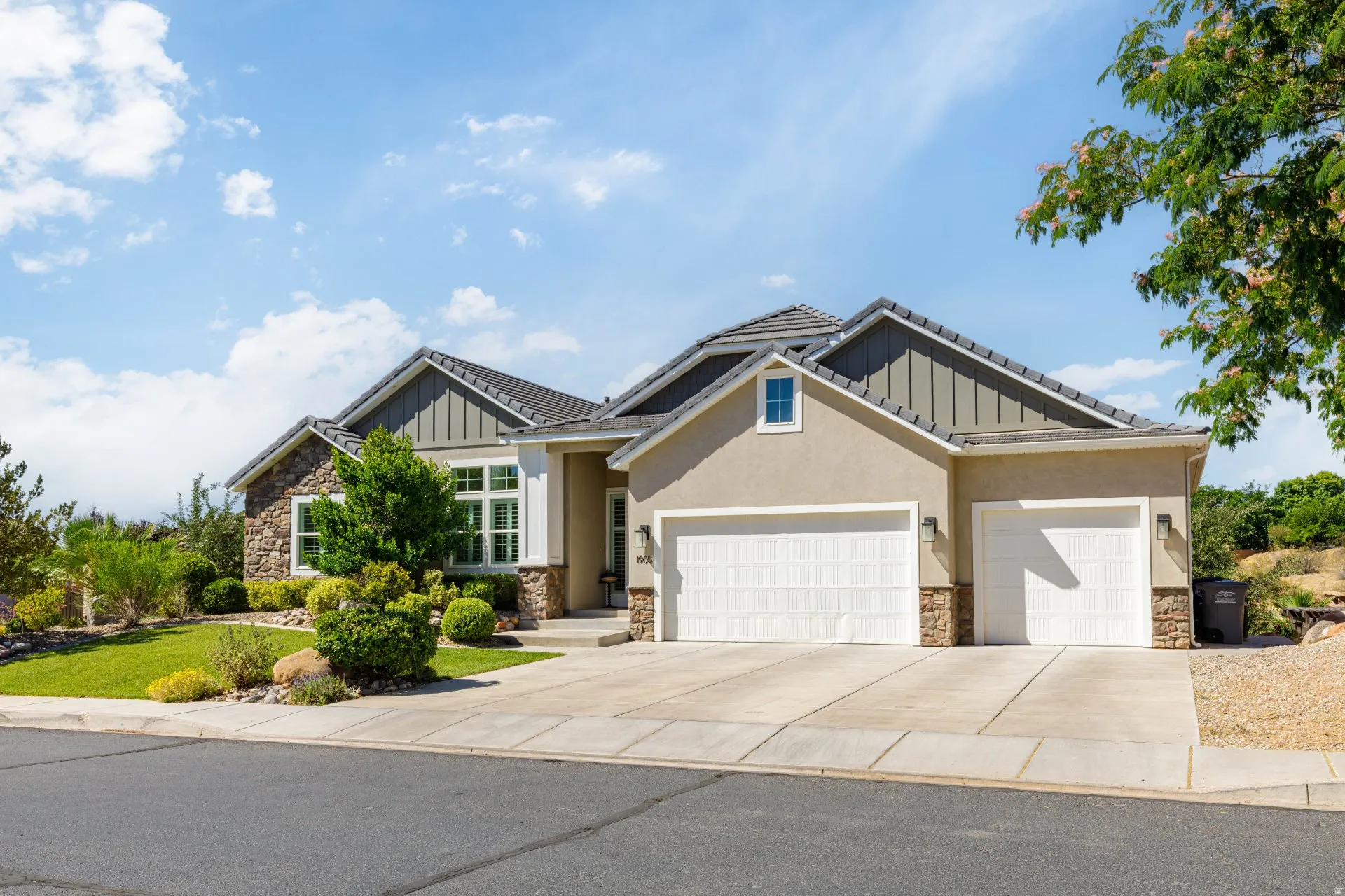 Contemporary stucco and stone exterior featuring a multi-gable roofline, two-car garage, established front landscaping, and a concrete driveway