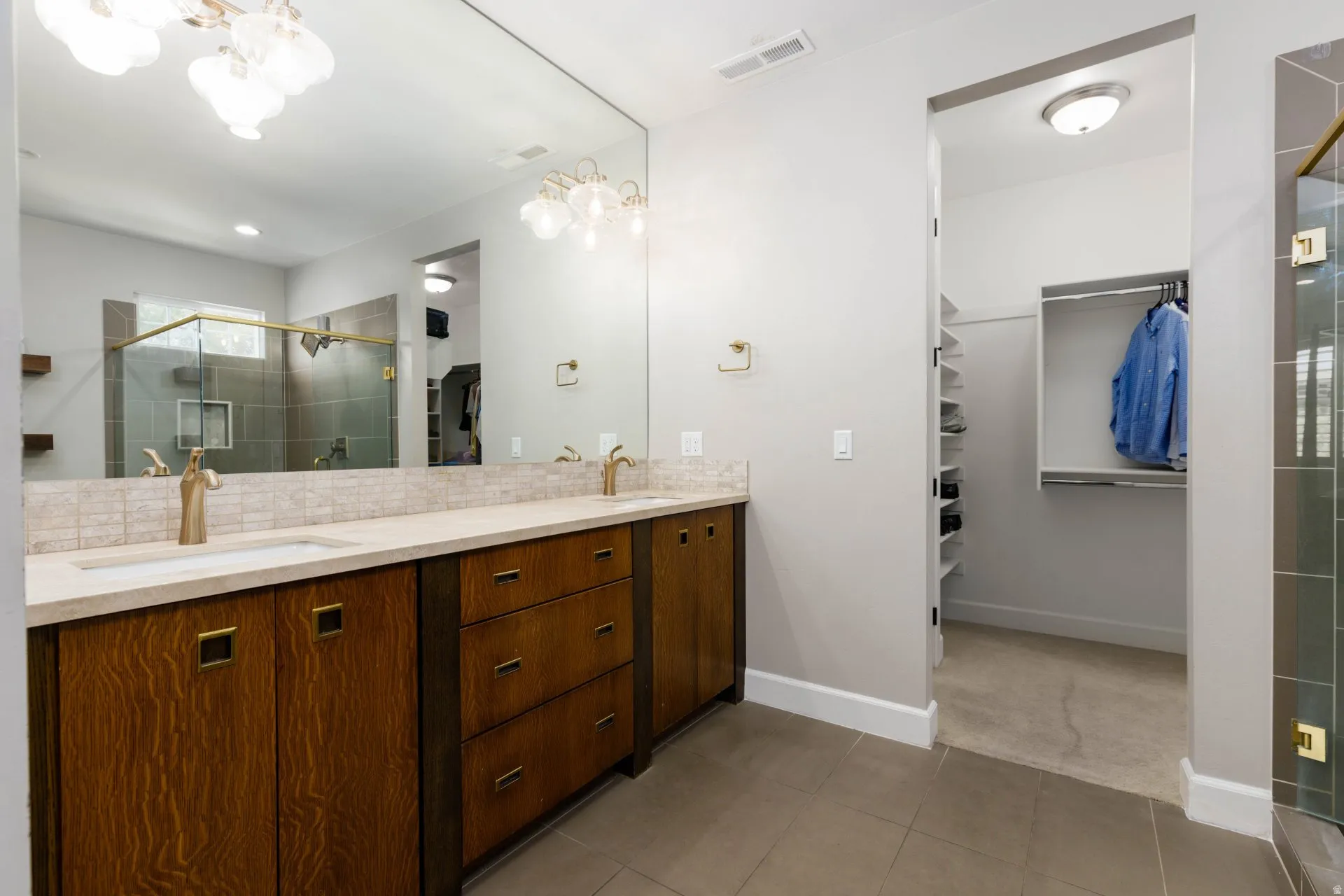 Bathroom vanity featuring dual under-mount sinks, wood-finish cabinetry with brass hardware, and a full-width mirror