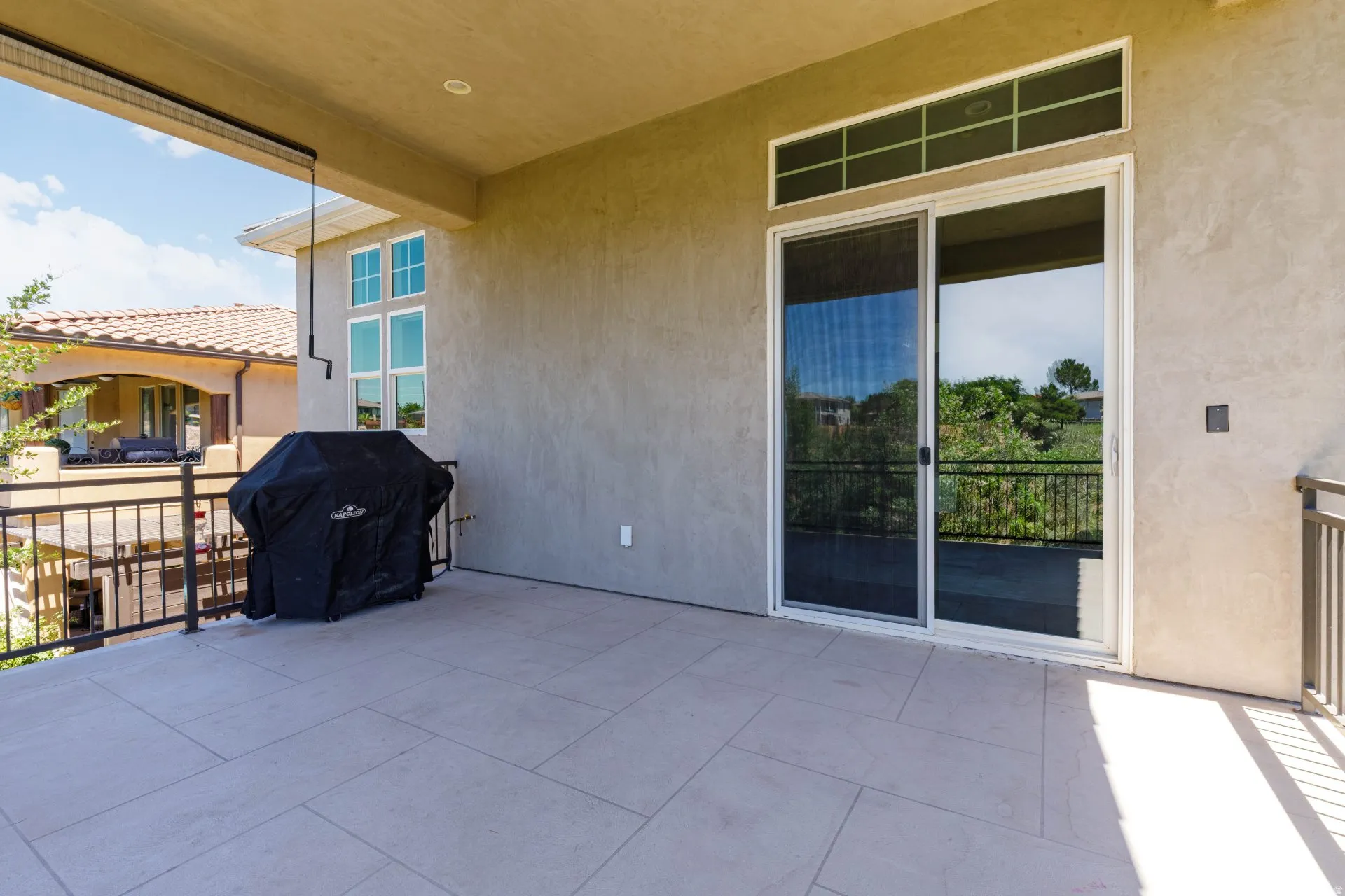 Spacious outdoor balcony featuring a neutral tile floor, stucco exterior, and a sliding glass door with transom windows