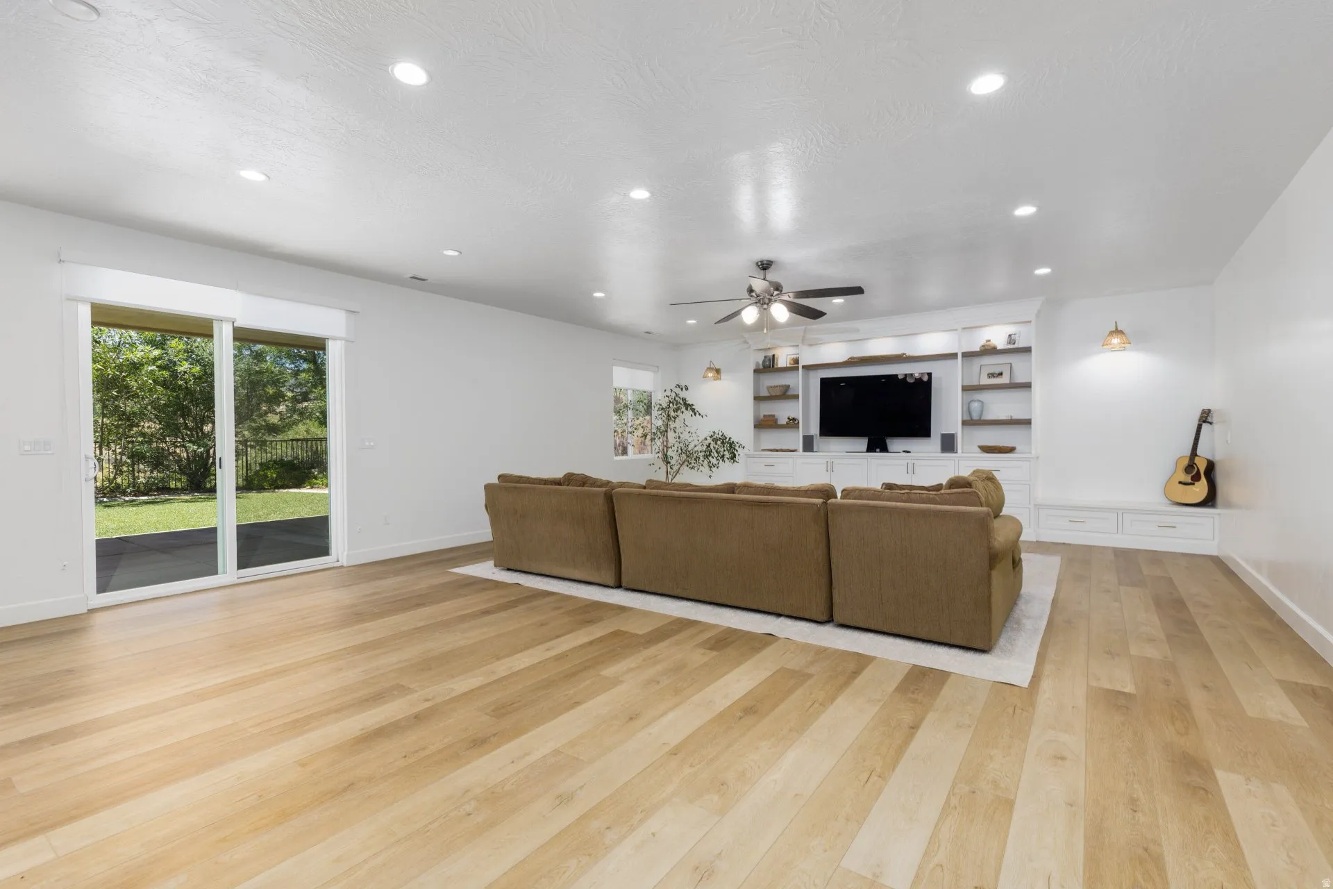 Spacious living area featuring wood-finish flooring, recessed lighting, and a built-in entertainment center with shelving