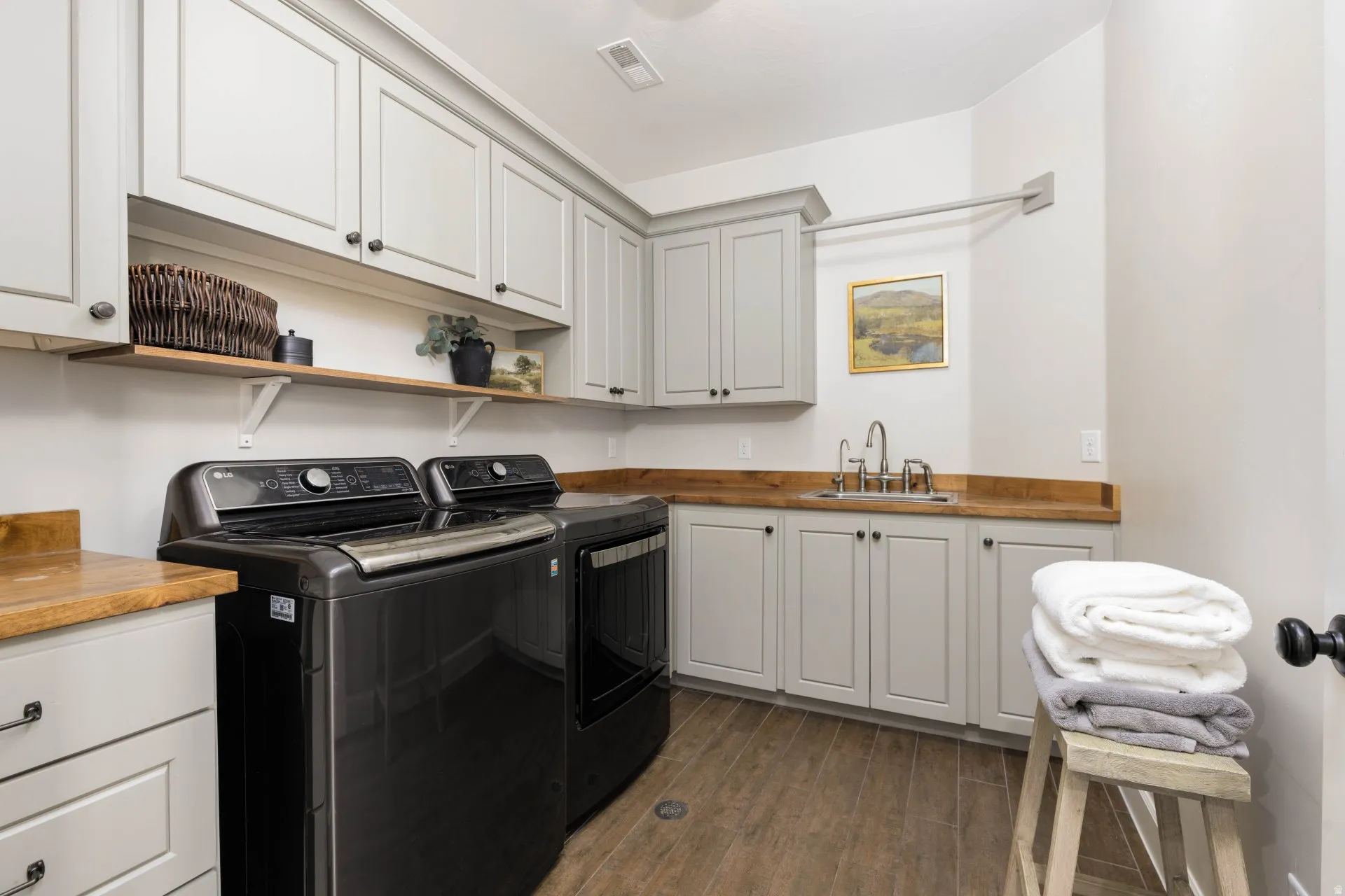 Laundry area featuring wood-finish flooring, light-toned cabinetry with dark hardware, and solid wood countertops