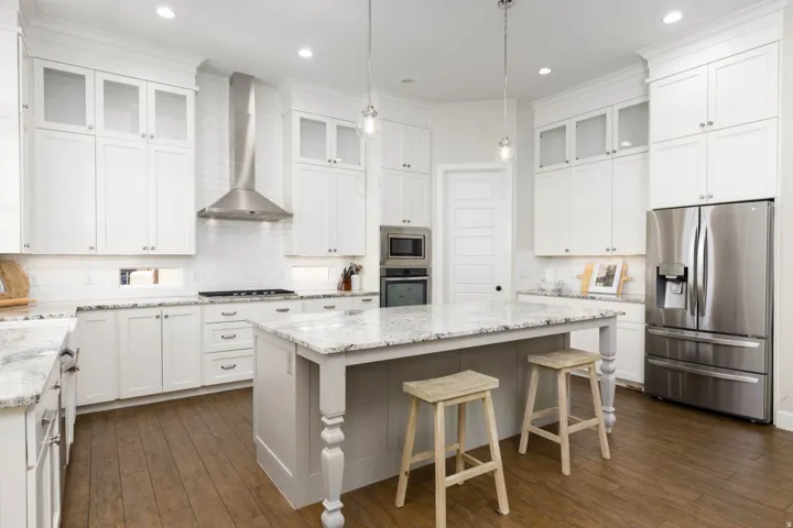 Bright kitchen featuring white cabinetry, granite countertops, a central island, stainless steel appliances, and wood-finish flooring