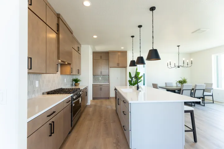 Modern kitchen featuring a gas range, a central island with integrated sink, wood-finish flooring, and pendant lighting