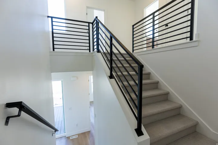 Staircase with light gray carpeting and matte black horizontal bar railings