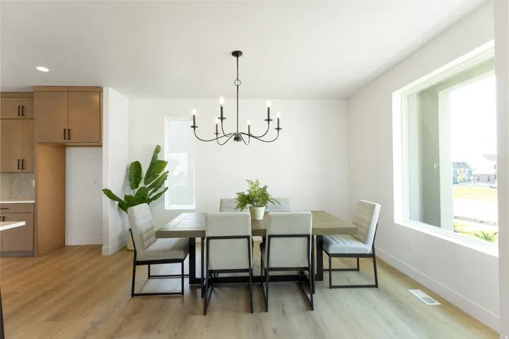 Open-concept dining area featuring wood-finish flooring, a contemporary chandelier, large windows, and built-in cabinetry