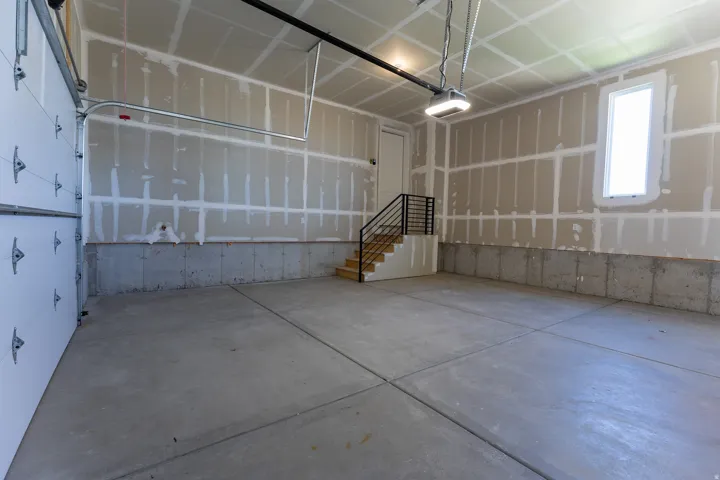 Spacious garage featuring a concrete floor, an overhead garage door, a staircase with a black metal railing, and a side door for interior access
