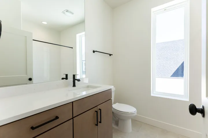 Modern bathroom featuring a wood-finish vanity with ample storage, a white countertop, a rectangular undermount sink, a matte black faucet, and a large mirror