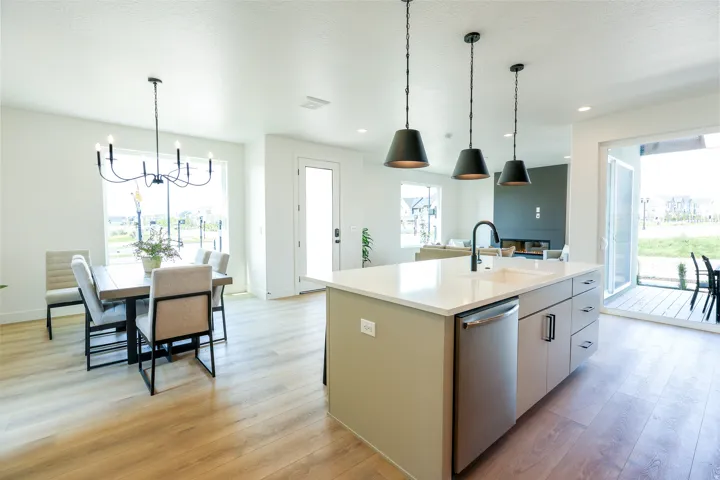 Open concept floor plan featuring wood-finish flooring, a kitchen island with sink and stainless steel dishwasher, and a dining area with chandelier lighting