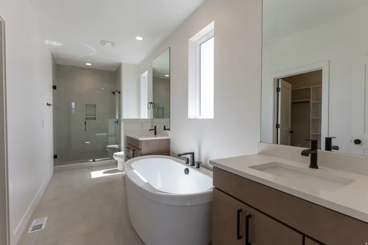 Contemporary Primary bathroom featuring a freestanding oval tub, a glass-enclosed shower with tile surround, dual wood-finish vanities with integrated sinks, and matte black fixtures
