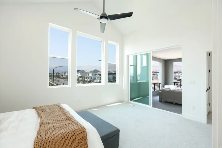 Vaulted ceiling with a contemporary ceiling fan, multiple tall windows, light-toned carpeting, and a glass sliding door