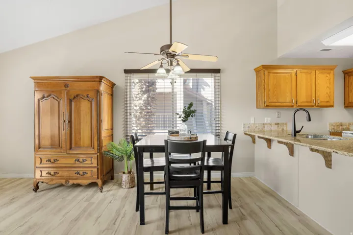 Vaulted ceiling dining area featuring wood-finish flooring, a ceiling fan with integrated lighting, and a window with horizontal blinds