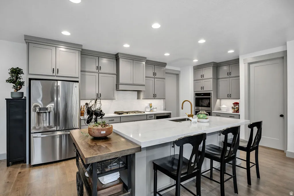 Expansive kitchen featuring a large central island with a light-toned countertop, ample gray cabinetry, stainless steel appliances, wood-finish flooring, and recessed lighting