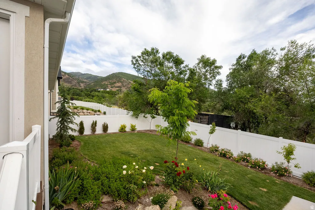 Expansive backyard featuring a manicured lawn, established landscaping, and a white privacy fence