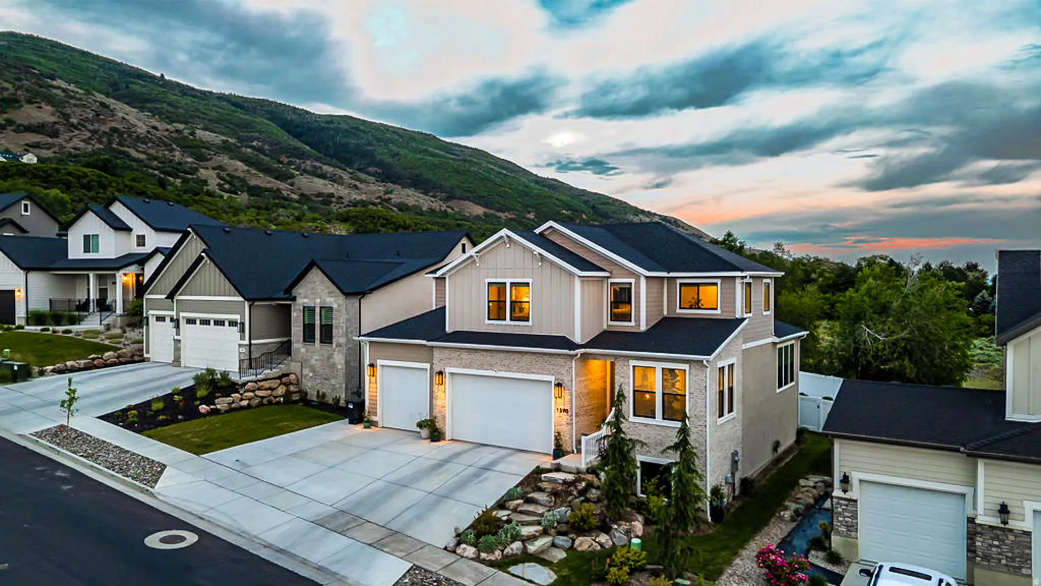 Contemporary architectural style with a stone and siding facade, featuring a two-car garage, established landscaping, and a mountain backdrop