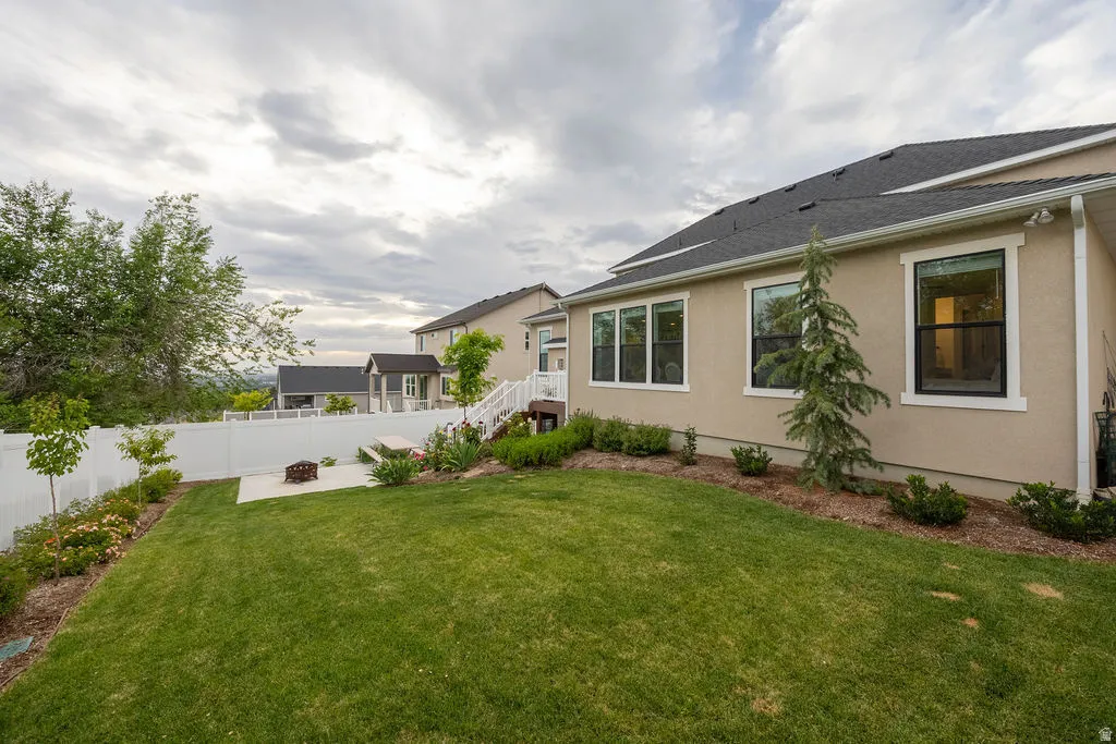 Expansive backyard featuring a manicured lawn, concrete patio with a built-in fire pit, and white vinyl fencing