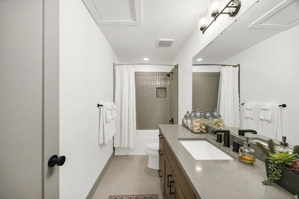 Bathroom featuring a large vanity with an integrated sink and matte black fixtures, a full-width mirror, tile flooring, and a bathtub with tiled surround and shower niche
