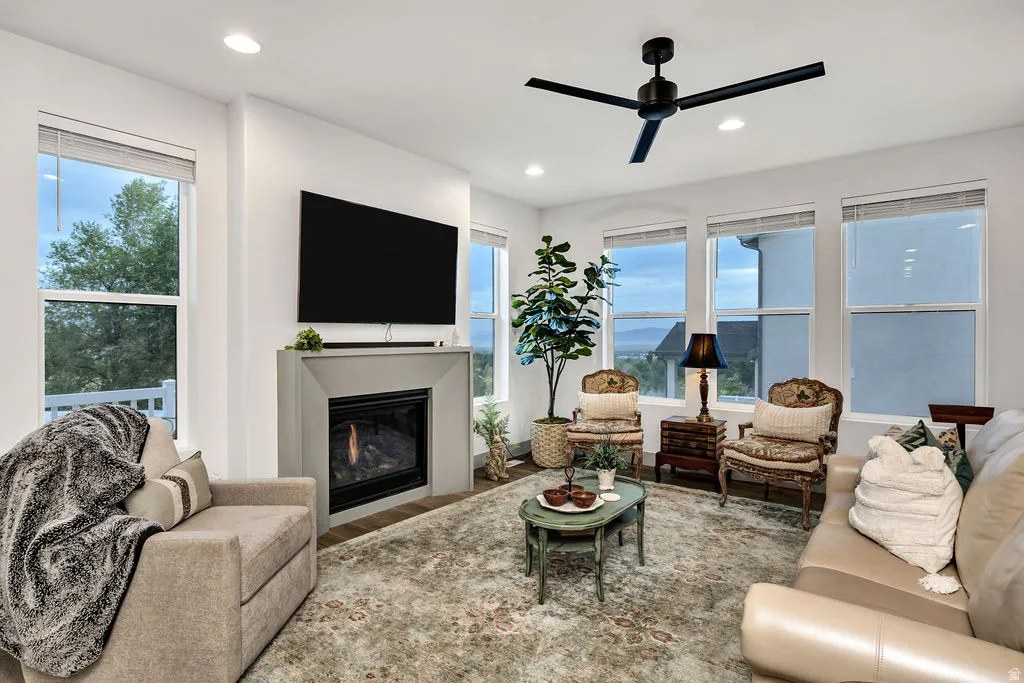 Living area featuring a modern fireplace with a light gray surround, multiple large windows, recessed lighting, and a contemporary black ceiling fan
