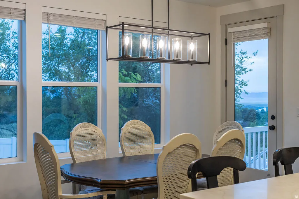 Dining area with a linear chandelier, multiple windows, and a glass-paned door opening to an exterior railing