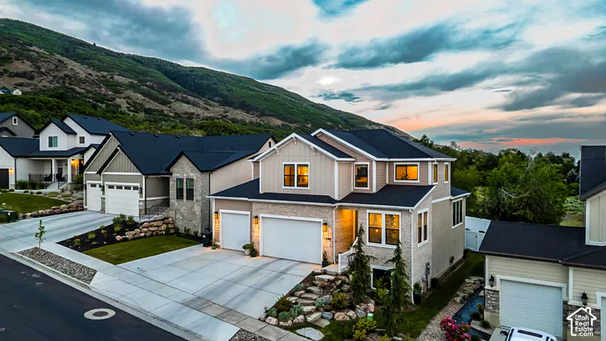 Contemporary architectural style with a stone and siding facade, featuring a two-car garage, established landscaping, and a mountain backdrop