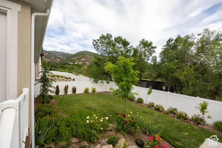 Expansive backyard featuring a manicured lawn, established landscaping, and a white privacy fence