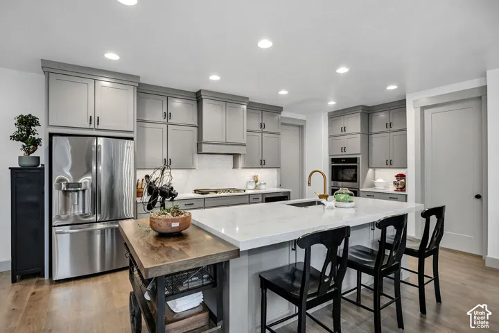 Expansive kitchen featuring a large central island with a light-toned countertop, ample gray cabinetry, stainless steel appliances, wood-finish flooring, and recessed lighting